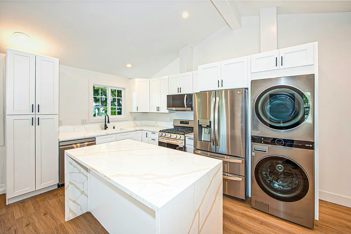 Kitchen in the Avenida De Los Arboles ADU by Yeganeh Inc., with a stone island, shaker cabinetry and a stacked washer and dryer