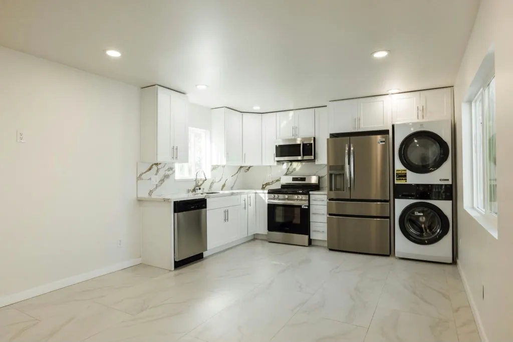 Kitchen in the Encino detached ADU by Yeganeh Inc., with white cabinetry, a marble-look backsplash and a stacked washer and dryer
