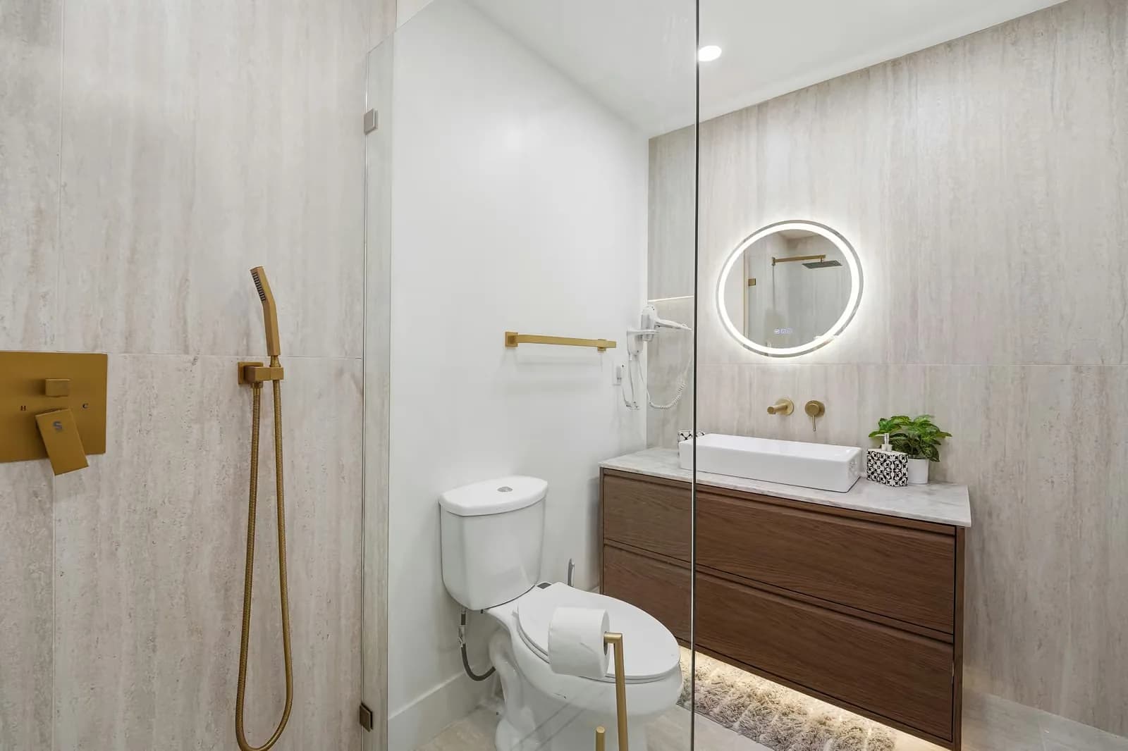 ADU bathroom with a floating wood vanity, a lit round mirror and brass fittings