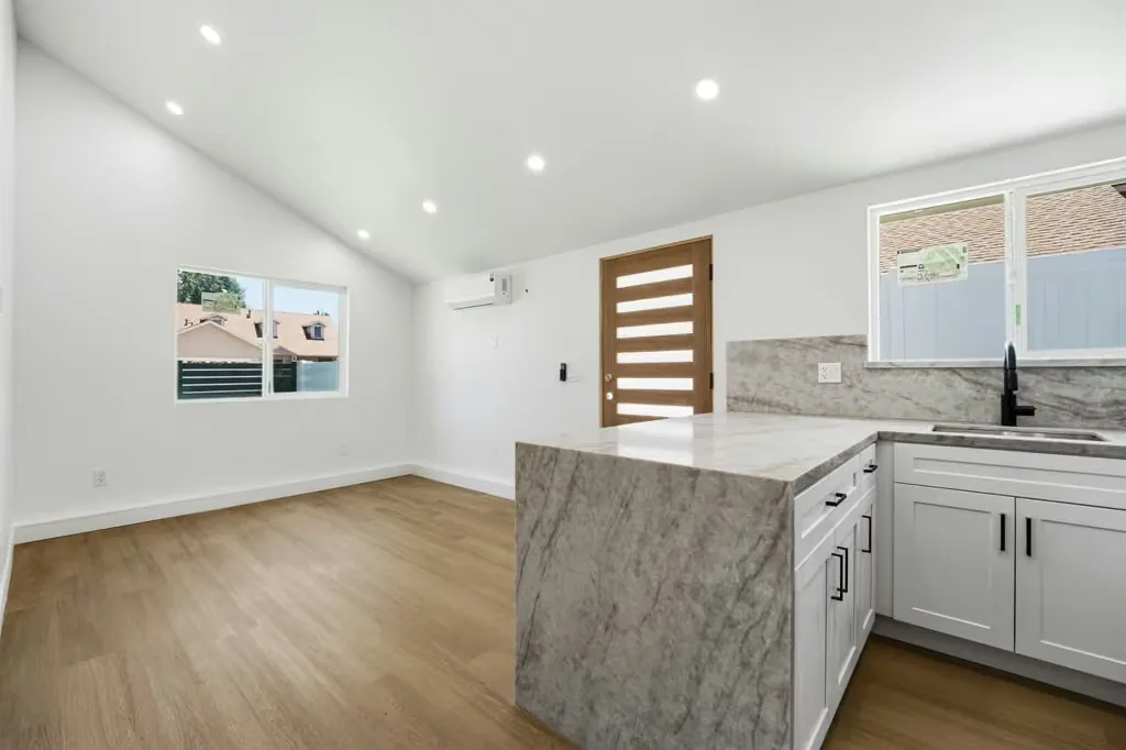 ADU kitchen with a stone peninsula, white cabinetry and a slatted timber entry door