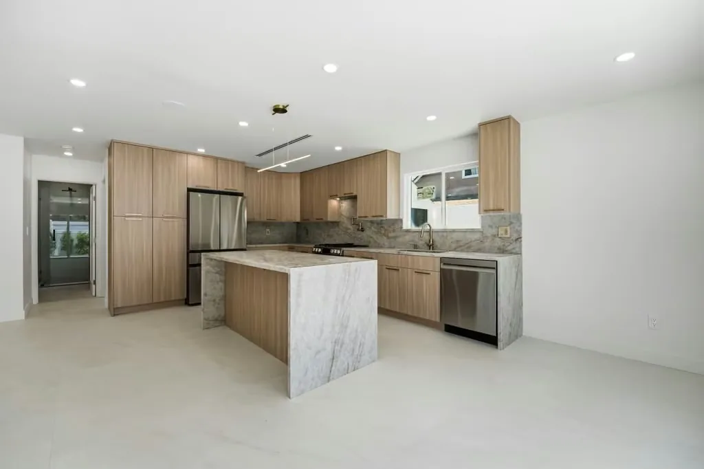 Compact ADU kitchen with wood cabinetry, a stone island and integrated appliances