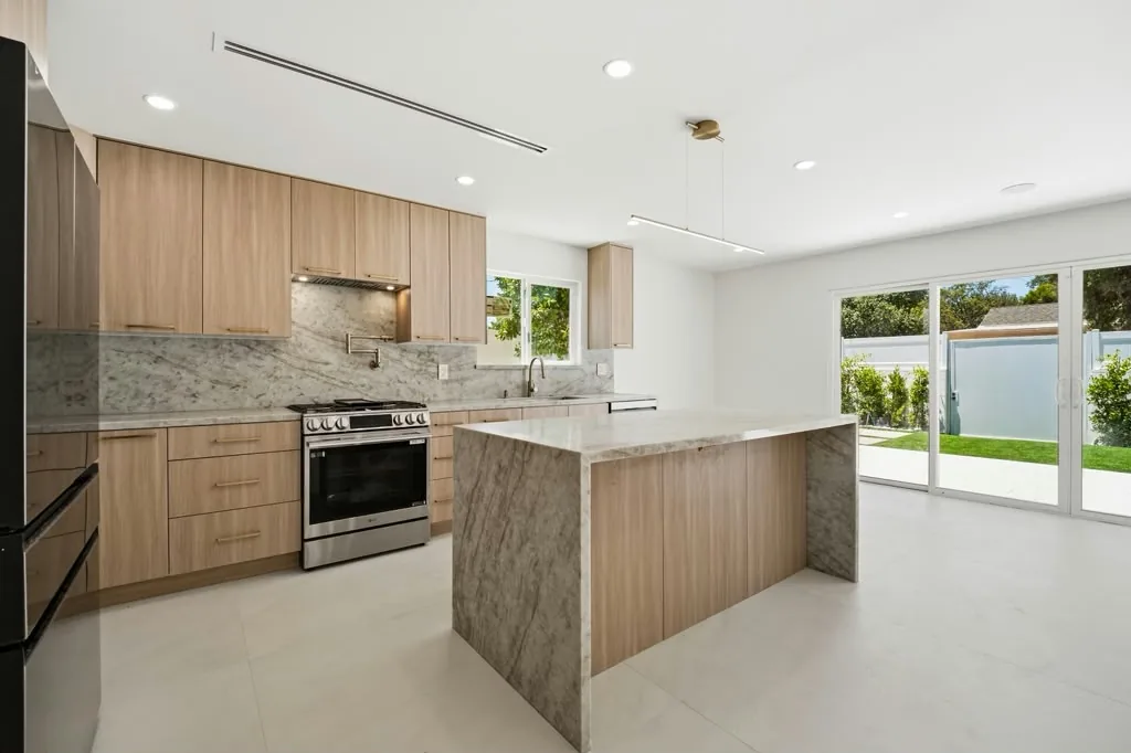 Kitchen at the Quakertown project by Yeganeh Inc., with a stone island, wood cabinetry and sliding doors onto the yard